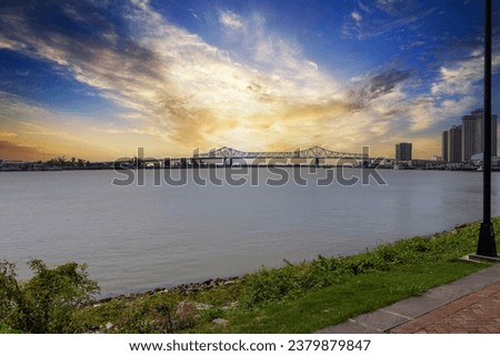 a gorgeous summer landscape along the Mississippi River with the Crescent City Connection bridge over the water with powerful clouds at sunset in New Orleans Louisiana USA