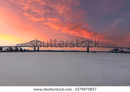 a gorgeous summer landscape along the Mississippi River with the Crescent City Connection bridge over the water with powerful clouds at sunset in New Orleans Louisiana USA