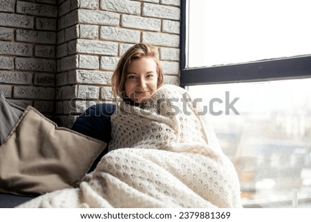 Wrapped in a cozy white blanket, a young woman smiles gently at the camera. The image embodies the essence of comfort and serenity, evoking a sense of calm Royalty-Free Stock Photo #2379881369