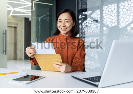 Successful satisfied business woman received mail envelope letter with good news message, Asian woman at workplace reading document paper, smiling at workplace inside office. Royalty-Free Stock Photo #2379888189