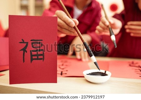 Closeup of Asioan family doing traditional calligraphy together with focus on hand drawn Fu character on red, copy space Happiness inscription