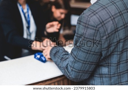 Process of checking in on a conference congress forum event, registration desk table, visitors and attendees receiving a name badge and entrance wristband bracelet and register electronic ticket
 Royalty-Free Stock Photo #2379915803