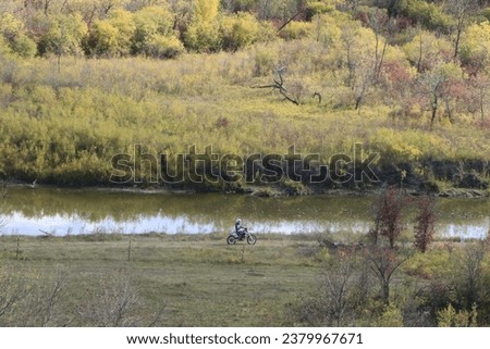 Dirt bike riders racing through valley with autumn foliage in background