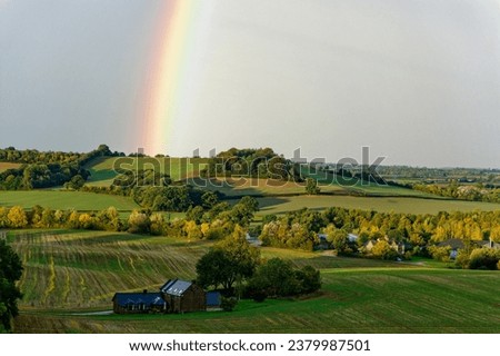 A beautiful rainbow over a green land with trees and barn