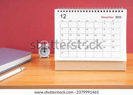 December Monthly desk calendar for 2023 year and alarm clock on wooden table.