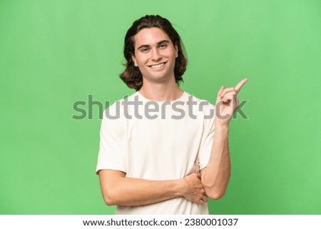 Young caucasian man isolated on green chroma background happy and pointing up Royalty-Free Stock Photo #2380001037