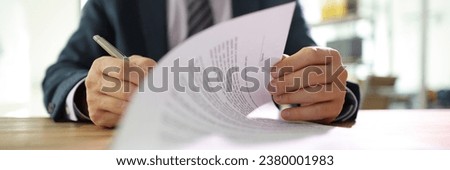 Businessman flips page of contract signing with pen after reading. Man in classic suit puts signature on paper sheet making successful deal