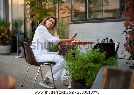 Portrait of a young attractive business woman sitting at a table in a cafe and texting on the phone, taking a selfie and browsing social networks