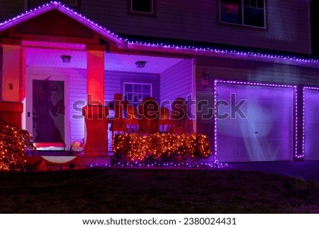 Illuminated Halloween house outdoor decorations with orange and purple garlands, witch silhouette, pumpkins and grave stones near the house porch Royalty-Free Stock Photo #2380024431