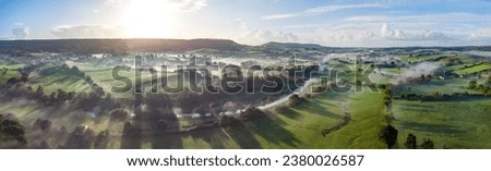 Aerial panorama picture of the river Otter near Honiton and Ottery St Mary. Sunrise with lens flare and rolling mist cross the lush green fields below. Spectacular landscape. 
