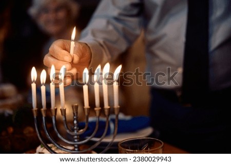 Close up of Jewish senior man lights candles in menorah during Hannukah celebration at home.  Royalty-Free Stock Photo #2380029943