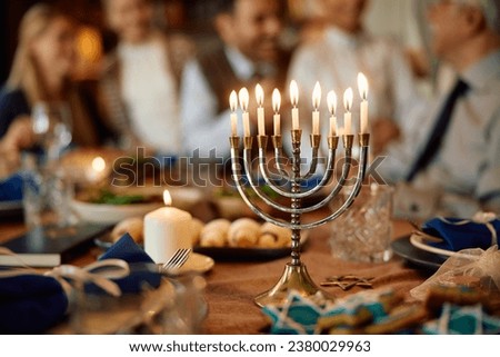 Lit menorah with multigeneration family in the background during Hanukkah celebration. Royalty-Free Stock Photo #2380029963