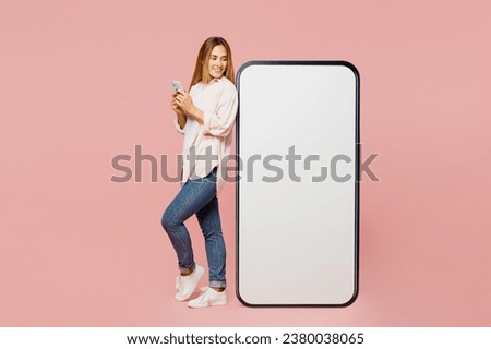 Full body side view young woman she wearing shirt white t-shirt casual clothes look at big huge blank screen mobile cell phone with area use smartphone isolated on plain pastel light pink background