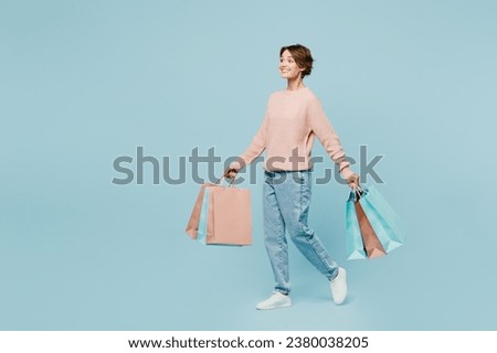 Full body young woman wear beige knitted sweater casual clothes hold paper package bags after shopping go isolated on plain light pastel blue background background. Black Friday sale buy day concept