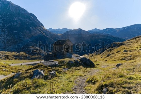 Small stone chapel with standing stone flag with cross at the south side of Swiss Gotthard Pass on a sunny late summer day. Photo taken September 10th, 2023, Gotthard Pass, Switzerland.
