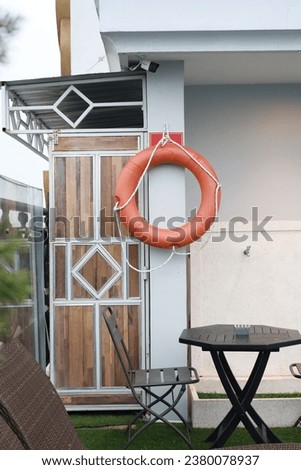 Lifebuoy is hung on the wall in the garden where there are tables and chairs with a green grass floor