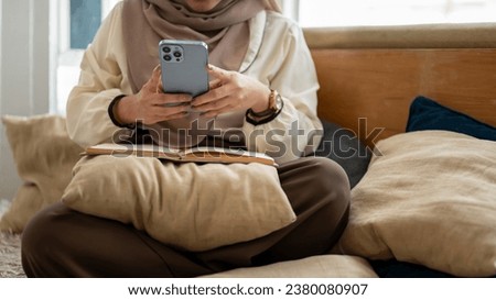 Cropped image of an Asian-Muslim woman using her smartphone while relaxing in a living room. chatting, responding to messages, online shopping, updating her social media