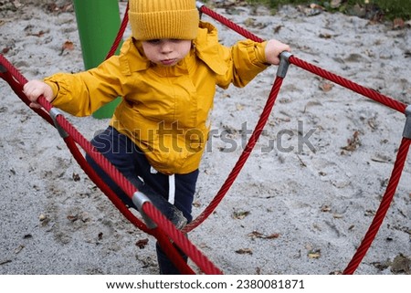 Little caucasian boy climbing and playing on a playground, outdoors autumn weather  Royalty-Free Stock Photo #2380081871