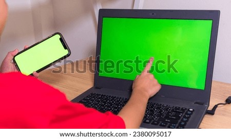 rear view of children who uses a smartphone and points at the laptop screen with the other to play games at home green screen prototype Independent work space people and technology Copy space and prod