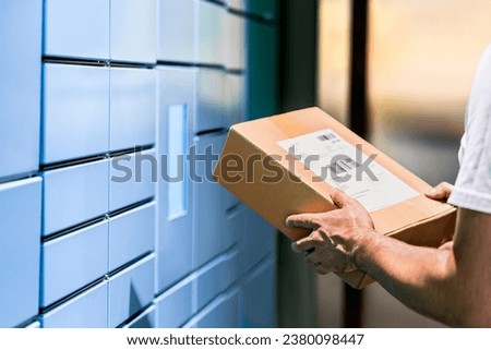 Parcel locker and package delivery service machine. Collect packet at mail storage station at post office. Man holding a box in hand. Blue shipment terminal automat pick up. Courier or customer. Royalty-Free Stock Photo #2380098447