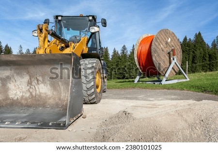 Wooden reel with orange fiber optic cable for fast expansion of internet with excavator in rural area in the Alps Royalty-Free Stock Photo #2380101025