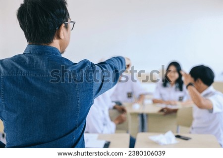 Asian male teacher angry and pointing at noisy students in classroom Royalty-Free Stock Photo #2380106039