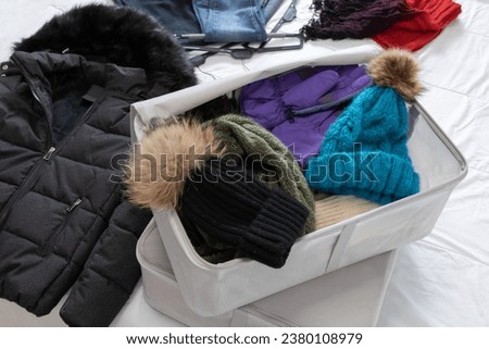 Horizontal photo, winter clothes on a bed, woolen hats and scarf, tucked in cloth boxes to be collected by the beginning of spring. Closet change.