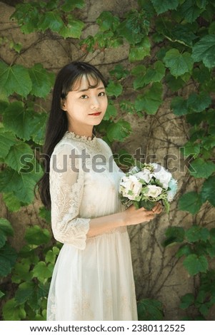 Wedding photo of a beautiful young woman standing in a forested park wearing a wedding dress and holding a bouquet