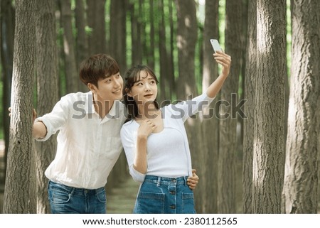 A lovely young couple are having a great time taking pictures using their smartphones in a forested park.