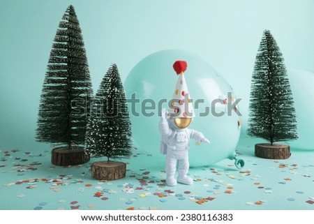 cosmonaut exploring a snowy forest like a new planet. They are surrounded by confetti, balloons and christmas tree. The composition is in turquoise-green color palette. Minimalist, trendy still life 