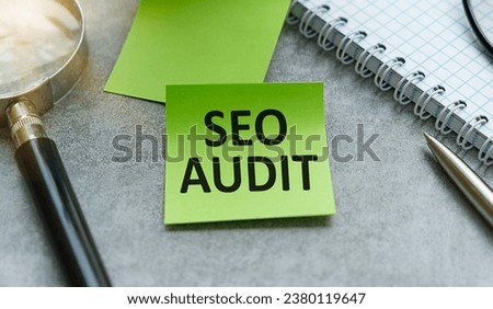 On a pink background, a magnifier, black paper clips and wooden blocks with the text SEO AUDIT. Business concept