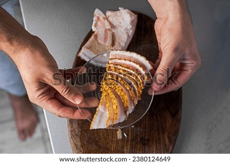 Use your hand to pick up thin pieces of chopped bacon on a cutting board and place on a plate. flatlay Royalty-Free Stock Photo #2380124649