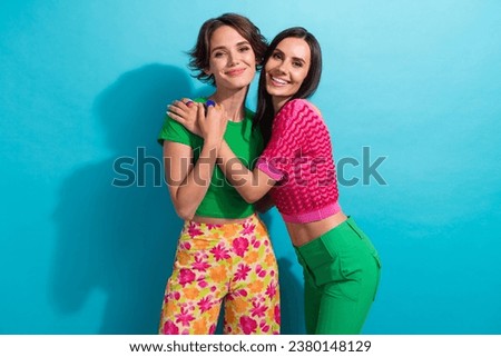 Photo of sweet cute ladies wear colorful clothes smiling embracing isolated blue color background