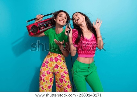 Photo of adorable funky ladies wear colorful clothes listening boom box music singing karaoke dancing isolated blue color background