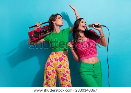 Photo of impressed cheerful girls dressed colorful outfits singing songs listening boom box music isolated blue color background