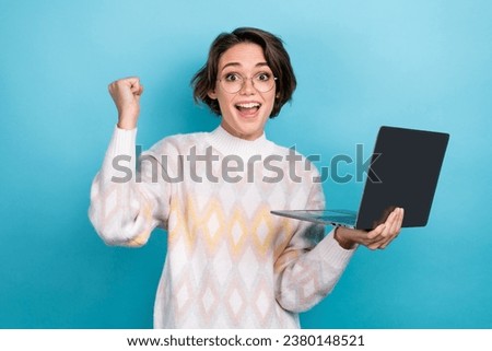 Photo portrait of lovely young lady raise fist excited hold laptop wear trendy white garment isolated on blue color background
