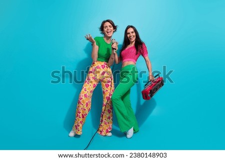 Full length body photo of two careless girls hold microphone with cassette recorder nostalgia concert isolated on blue color background