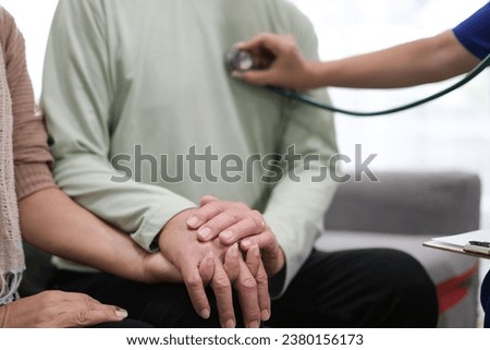 Caring young female doctor examining her contented senior patient with stethoscope in living room. Medical service for elderly, elderly sickness, declining health..