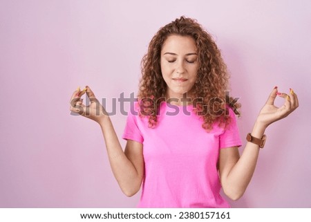 Young caucasian woman standing over pink background relaxed and smiling with eyes closed doing meditation gesture with fingers. yoga concept. 