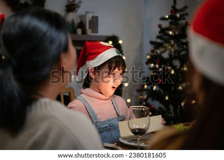 Cute little girl in Santa hat opening Christmas present and smiling.