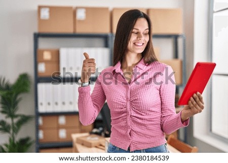 Young hispanic woman working at small business ecommerce doing video call with tablet smiling happy and positive, thumb up doing excellent and approval sign 
