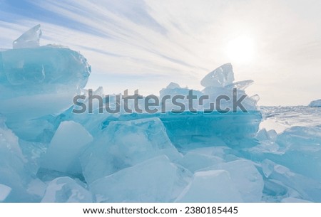 Winter cold natural background with pile of ice floes on frozen sea against sun and sky with layered clouds. Blue flat ice floe can serve as podium or pedestal for ad cosmetics products or food goods Royalty-Free Stock Photo #2380185445