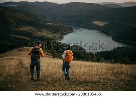 Two friends walking uphill with backpacks, catching sight of a serene lake Royalty-Free Stock Photo #2380185485