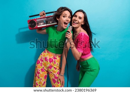 Photo of sweet impressed ladies wear colorful clothes listening boom box music singing microphone isolated blue color background