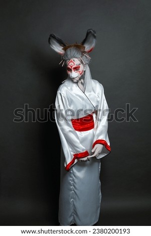 Young woman with animal makeup, mask and stage asian costume standing against black background. Halloween, carnival, performance and theater concept