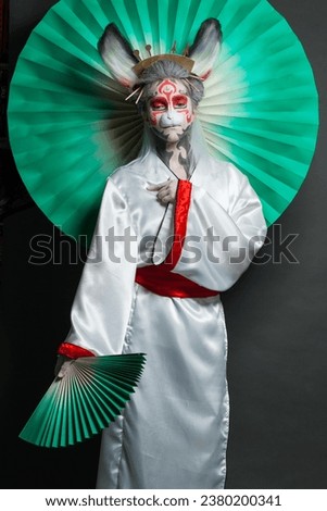 Creative theater actress with makeup and costume holding green fan on black background