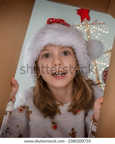 Cute child girl with a Santa hat opening a Christmas present. Happy holidays and New Year