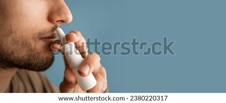 Man using nasal spray for a runny nose and congestion isolated on a blue background, close-up. Rhinitis, sinusitis, cold. Banner. Copy space Royalty-Free Stock Photo #2380220317