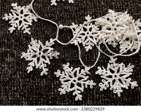 A pile of knitted white snowflakes in the form of a garland on a dark background. Snowflakes as a symbol of winter holidays create the right atmosphere and festive warm mood.