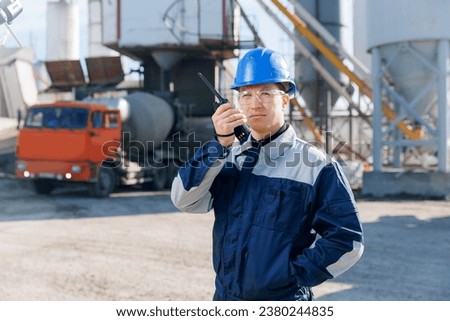 Building site, worker use radio set for control concrete mixer truck. Construction man in hardhat talking on walkie talkie on Industry cement factory.